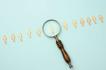 wooden men and a magnifying glass on a blue background. Recruitment concept, search for talented and capable employees, career growth, flat layの写真素材