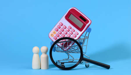 miniature metal shopping cart with calculator and wooden family, magnifying glass, the concept of budget control, spending on purchases, saving moneyの写真素材