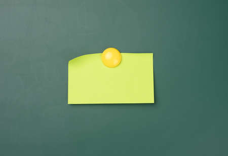 blank yellow sticker on a green chalk board attached by a round magnet, place for an inscription