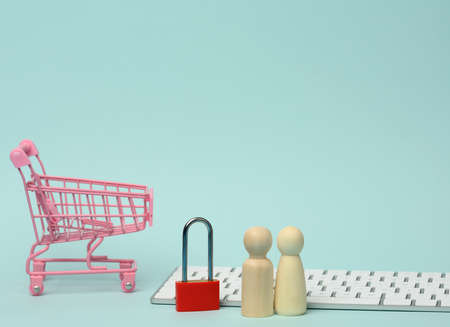 a red metal padlock stands on the keyboard and behind a miniature shopping cart, blue background. Personal data protection concept, secure online shoppingの写真素材