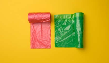 green and red plastic bags for trash can on yellow background, top view