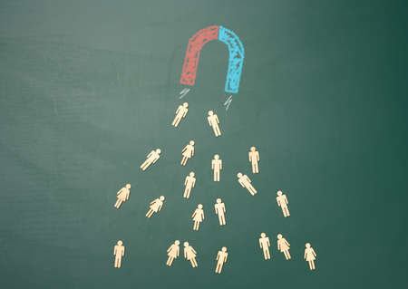 a group of wooden little men are attracted by a magnet on a green background. Personnel search concept, team recruitmentの写真素材