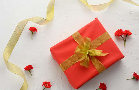 box packed in holiday red paper and tied with a silk ribbon on a background, birthday gift, surprise