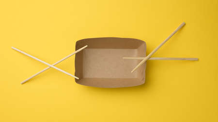 empty brown paper plate and wooden chopsticks on a yellow background, top view. Disposable...