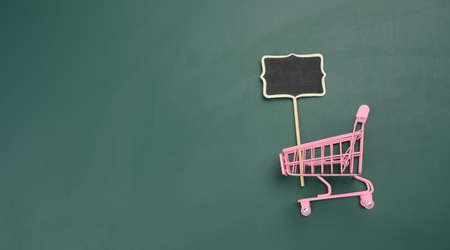 pink miniature shopping cart on green background. Seasonal sale, copy spaceの写真素材