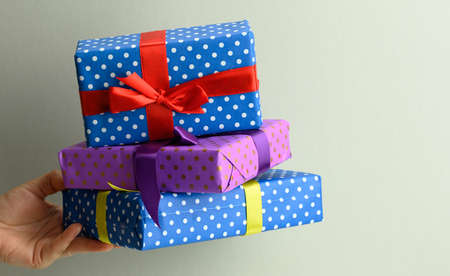 female hand holding a stack of gift boxes tied with silk ribbon on a gray background, surprise and...