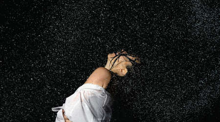 beautiful woman of Caucasian appearance with black hair dances in drops of water on a black...