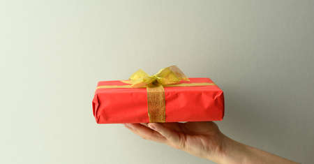 female hand are holding a red gift box on a gray background, happy birthday concept