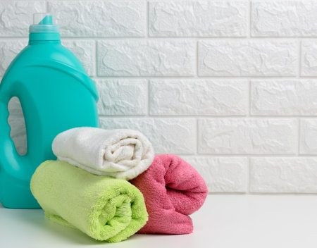a plastic bottle of liquid washing powder and folded towels on a white shelfの写真素材