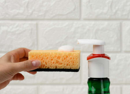 female hand holds kitchen sponge with white foam near plastic dispenser