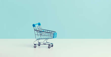 empty miniature shopping cart on a blue background. Seasonal sale, copy spaceの写真素材