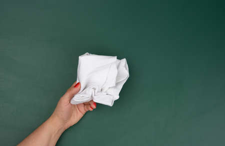 a woman's hand holds a white rag against the background of a green chalk board, a place for an inscriptionの写真素材