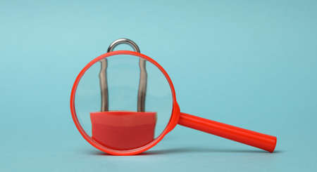 metal lock stands on a red plastic magnifying glass on a blue background. Data protection concept, personal informationの写真素材