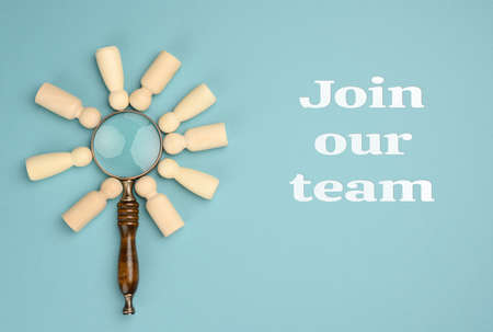 wooden men and a magnifying glass on a blue background. Recruitment concept, search for talented and...