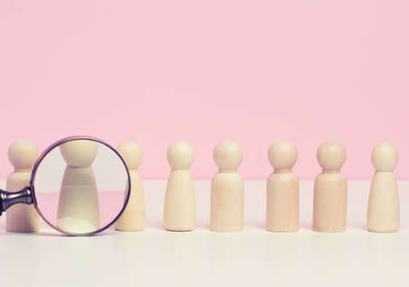 wooden figures of men stand on a pink background and a red plastic magnifying glass. Recruitment concept, search for talented and capable employees, career growthの写真素材