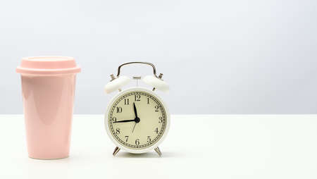 round retro alarm clock and pink ceramic cup with coffee on white table