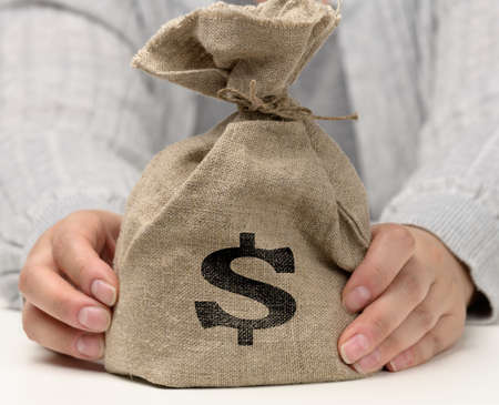 hand holds a canvas bag full of money with a US dollar icon on a white background. Budget planning concept, profit and savings, final financial resultの写真素材