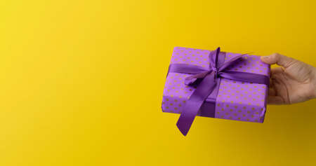 female hand are holding a purple gift box on a yellow background, happy birthday conceptの写真素材