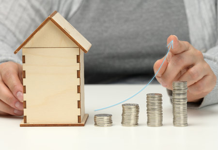 wooden model of a house, a stack of coins and an ascending graph. The man sits at the table. Higher...