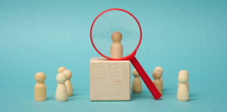 wooden figures of men stand on a beige background and a red plastic magnifying glass. Recruitment concept, search for talented and capable employees, career growthの写真素材