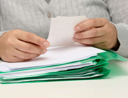 woman sitting at white table and holding paper check, budget analysis concept. Checking income and...