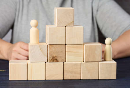 pyramids from wooden cubes and figurines of men on the table. The concept of achieving goals, moving...