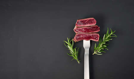 Fried pieces of beef on an iron fork on a black background. The degree of readiness is rare. View from above, copy spaceの写真素材