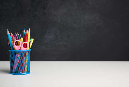 metal glass with pens, pencils and felt-tip pens and scissors on the background of an empty black...