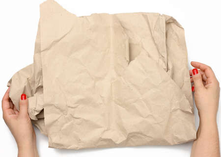female hands hold crumpled brown paper on white background, top viewの写真素材