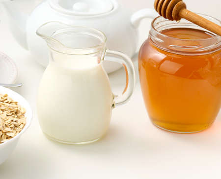 fresh milk in a transparent glass decanter and a jar of honey stand on a white table, a healthy product, breakfastの写真素材