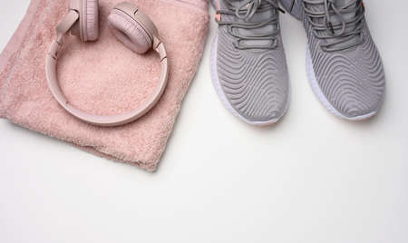 pair of gray textile sneakers, wireless headphones and a textile pink towel on a white background. Set for sports, running, top viewの写真素材