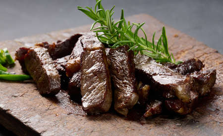roasted piece of beef ribeye cut into pieces on a vintage brown chopping board, rare doneness....
