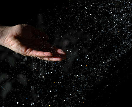 female hand and flying drops of water on a black backgroundの写真素材