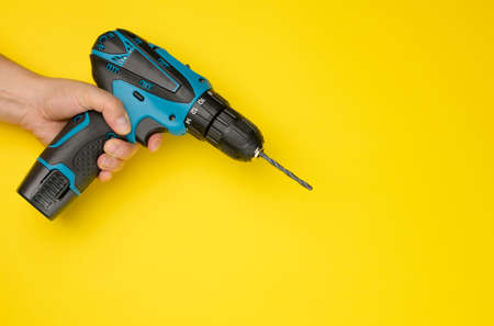 female hand holds a cordless drill on a yellow background. Tool for workの写真素材