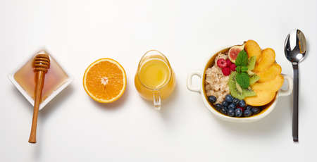 plate with oatmeal and fruit, half a ripe orange and freshly squeezed juice in a transparent glass decanter, honey in a bowl on a white table. Healthy breakfastの写真素材