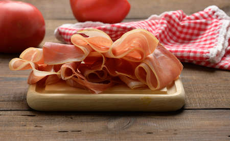 sliced thin slices of prosciutto on wooden brown board, wooden table backgroundの写真素材