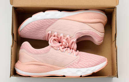 pair of pink textile sneakers in an open brown paper box on a white table, top view