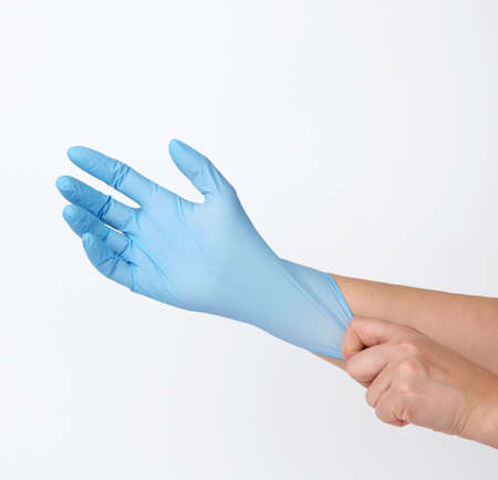 process of putting blue latex gloves on hand on white background, hygiene protector