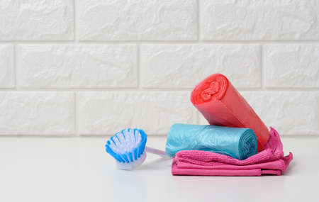 brush and stack of disposable plastic trash can bags on white table, white brick wall background, copy spaceの写真素材