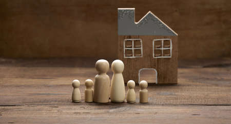 wooden family figurines, model house on a brown background. Real estate purchase, rental concept. Moving to new apartmentsの写真素材