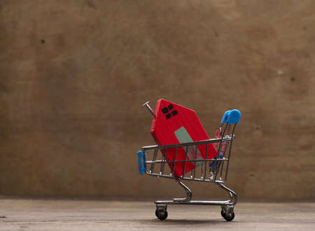 red wooden house in a metal miniature cart on a brown background. Real estate purchase concept, mortgageの写真素材