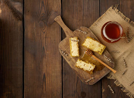 wax bee honeycomb with honey on wooden board and wooden spoon, brown table, copy space