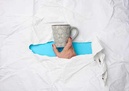 female hand holding a ceramic mug on a background of white torn paper, time to drink coffee and relaxの写真素材