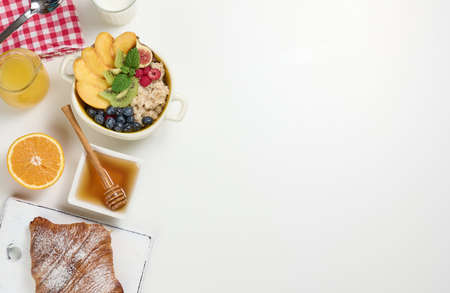 milk, plate with oatmeal porridge and fruit, freshly squeezed juice in a transparent glass decanter, honey in a bowl on a white table. Healthy breakfast, copy spaceの写真素材