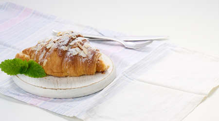 Baked croissant sprinkled with sugar on wooden board, white linen napkinの写真素材