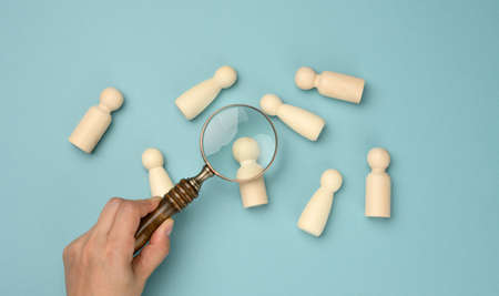 wooden men and a magnifying glass on a blue background. Recruitment concept, search for talented and capable employees, career growth, flat layの写真素材