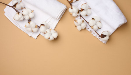 folded white cotton terry towel and sprigs of cotton flower on a light brown background, top view , copy spaceの写真素材