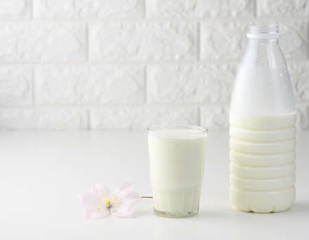 full plastic milk bottle and glass cup on white table, brick wall backgroundの写真素材
