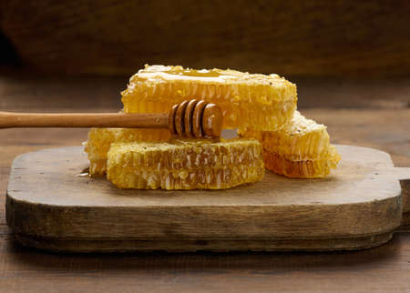 wax honeycomb with honey on a black board and a wooden spoon, brown tableの写真素材