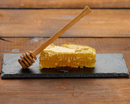 wax honeycomb with honey on a black board and a wooden spoon, brown table